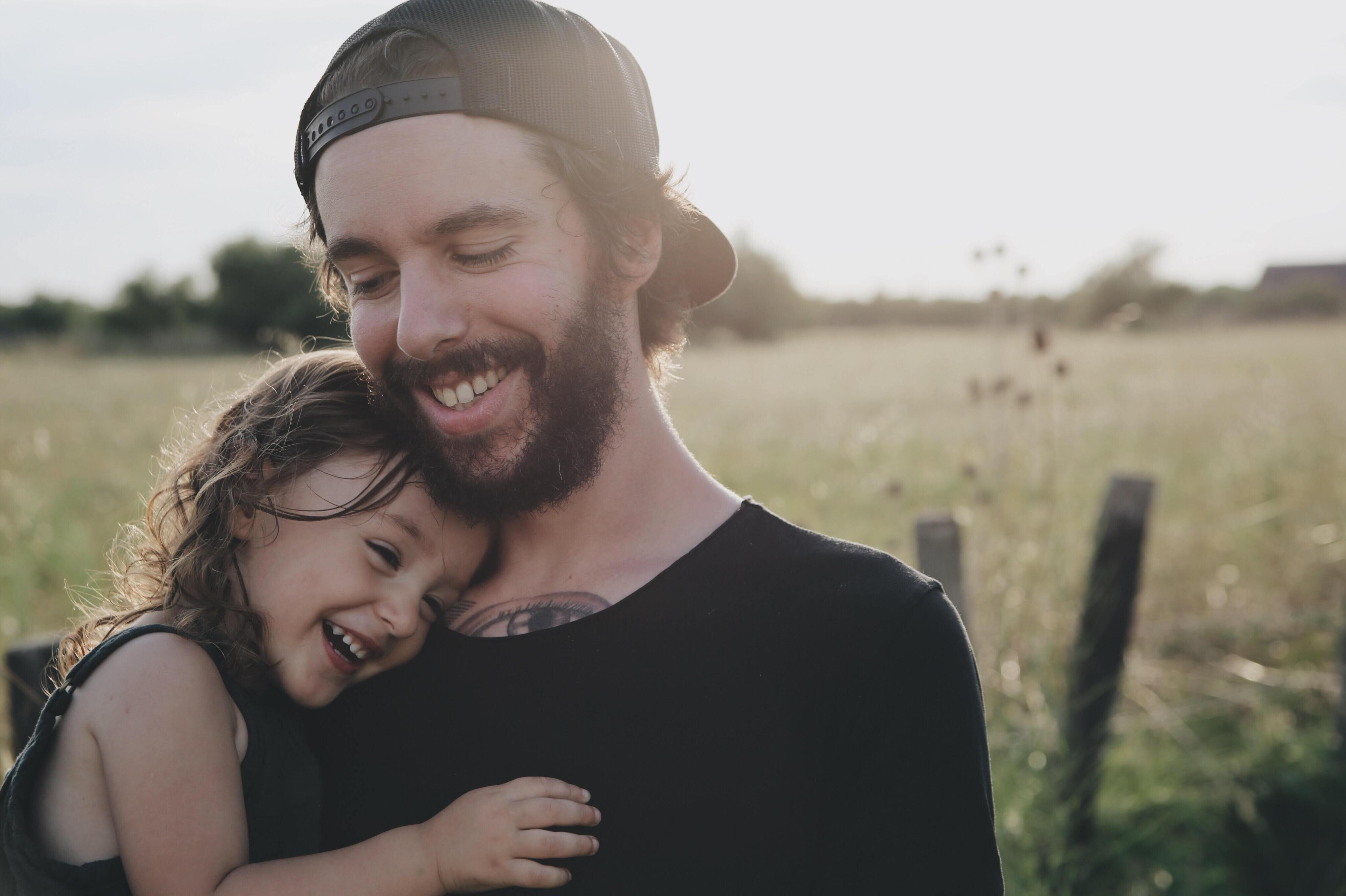 Smiling dad standing in field holding his smiling young daughter